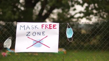Çitin üzerinde Maskesiz Bölge yazan bir poster. Kullanılmış cerrahi koruyucu maskeler yakınlarda asılı. Maske takmayı protesto et, maske karşıtı konsept