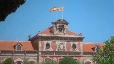 Barselona, Katalonya, İspanya - Temmuz 2018: İspanya ve Katalonya bayraklarıile Parlament de Catalunya binanın tepesinde rüzgarda çırpınan, kıpır kıpır yapraklı yeşil ağaçların arasından manzara.