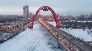 Alacakaranlıkta Moskva nehri üzerinde Pitoresk Köprü üzerinde uçan. Donmuş nehir üzerindeki ışıklı köprüde yoğun trafik havadan dolly çekim.