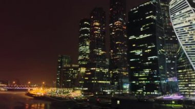 Işıklı pencereleri ile Moskova-şehir iş kuleleri Gece havadan çekim. Rıhtımda şehir trafiği var. Gece şehir aydınlatma yanıp sönen ışıklar.