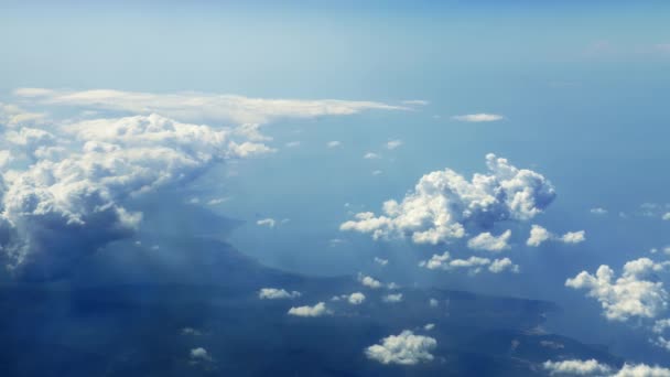 神聖な日光の下で積雲を通して海沿岸に沿って飛行します 飛行機の窓から雲を照らす美しい薄暗い太陽の光を持つ田舎の海岸線までの美しい眺め — ストック動画
