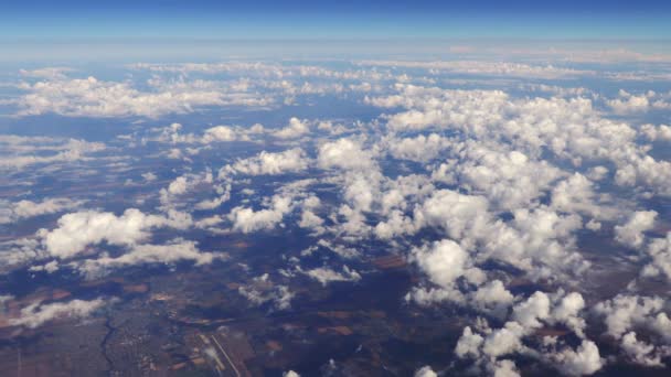 Letí přes nádherné hromady bílých mraků, které se tiše pohybují zprava doleva na jasně modrém nebi a hluboko pod nimi krajiny. Malebný výhled z okna letadla.