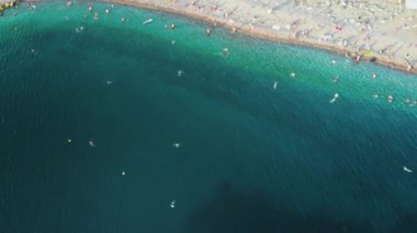 Yaz akşamı plaj ve Soçi Olimpiyat Parkı'na güzel havadan manzara. Denizin, yolların, park tesislerinin ve dağların tüm panoramasını gösteren, sudan yukarı doğru hareket eden kamera.