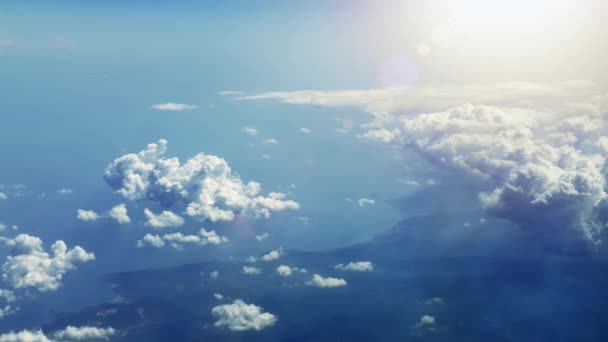 在纯净的阳光下 在蓬松的云层中沿着海岸飞行 从飞机窗口到乡村海岸线的风景如画的景色 阳光闪耀在云层上 光线和镜头耀斑 — 图库视频影像