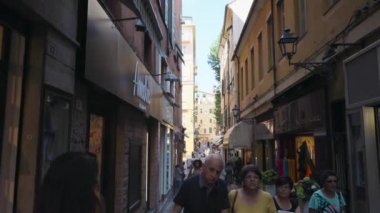 Sanremo, İtalya - Temmuz 2018: Loş ışıkta renkli vitrinler ve kafelerile dar Avrupa caddesi boyunca ilerleyen kamera. İnsanlar yavaş çekimde dolaşıyor.