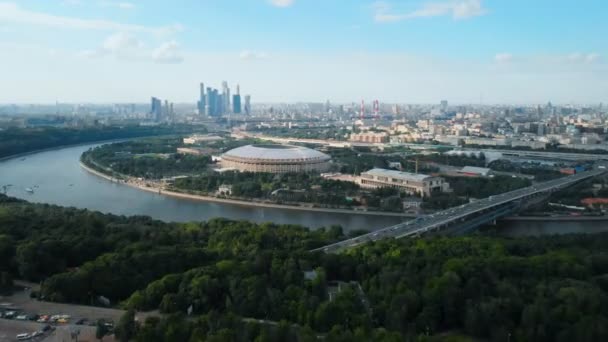 モスクワ川の上の大きな近代的なスタジアムに向かって飛ぶタイムラプス 広い都市の大通りに集中的なトラフィック 地平線上の明るい青空とモスクワ市の塔 — ストック動画