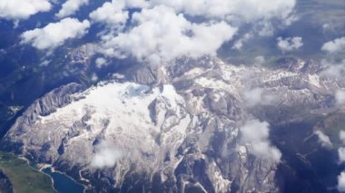 Çok altında göller ve nehirler ile yeşil vadiler ile çevrili güzel karla kaplı zirveleri üzerinde uçan. Kabarık bulutlar ile uçak penceresinden pitoresk kar dağ manzara görünümü.