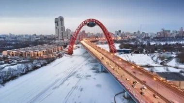 Alacakaranlıkta Moskva nehri üzerindeki Pitoresk Köprü'den uçuyor. Donmuş nehir üzerindeki ışıklı köprüde yoğun trafik havadan hızlandırılmış dolly çekim.