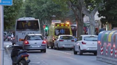 Salou, Katalonya, İspanya - Temmuz 2018: Sarı ambulans üzerinde flaşör ile şehir yolunda. İlk yardım görevlisi araba etrafında meşgul, şehir trafiği geçen, insanlar arka planda ve ön planda hareket.