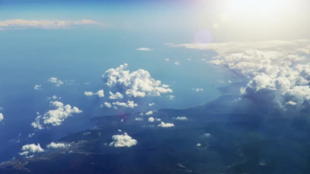 在纯净的阳光下 在蓬松的云层中沿着海岸飞行 从飞机窗口到乡村海岸线的风景如画的景色 阳光闪耀在云层上 光线和镜头耀斑 — 图库视频影像