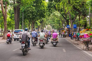 Hanoi, Vietnam - 27 Ekim 2017: Hanoi sokakta motor bisiklet sürme insanlar. Sokağın taşkın dallar yeşil ağaçlar.