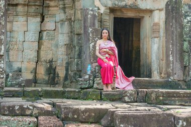 Angkor, Kamboçya - 17 Kasım 2017: Kamboçya geleneksel kıyafet girişinde Bayon Tapınağı'nda oturan kız. Kamboçya Angkor Thom zengince dekore edilmiş Khmer tapınakta olduğunu