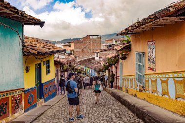 Guatape, Kolombiya 27 Mart 2018 turistler tarafından renkli koloni evler bir Arnavut kaldırımlı sokak Guatape, Antioquia Kolombiya içinde yürürken.