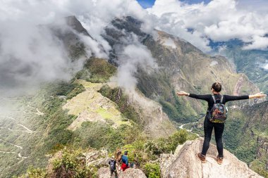 Cusco, Peru 6 Nisan 2019 Wayna tepesinde duran kız, Huayna Picchu zirvesi Machu Picchu, İnka şehir kompleksi ve Machu Picchu dağ zirvesi arka planda.