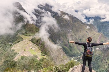 Cusco, Peru 6 Nisan 2019 Wayna tepesinde duran kız, Huayna Picchu zirvesi Machu Picchu, İnka şehir kompleksi ve Machu Picchu dağ zirvesi arka planda.