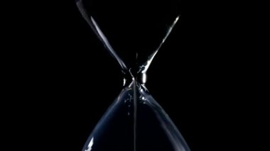 Kum saati siyah arka plan ve ortalanmış bileşiminde yanal ışık arka ışık ile kum akışında