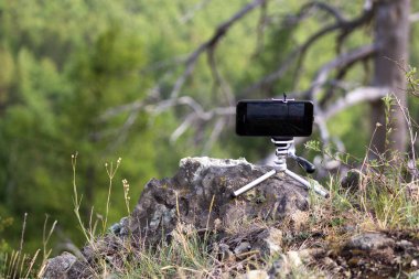 Doğanın arka planında bir tripodun üzerinde akıllı telefon.