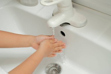 Enfeksiyonu önlemek için eve döndükten hemen sonra ellerini akan suyla yıkayan çocukların elleri.