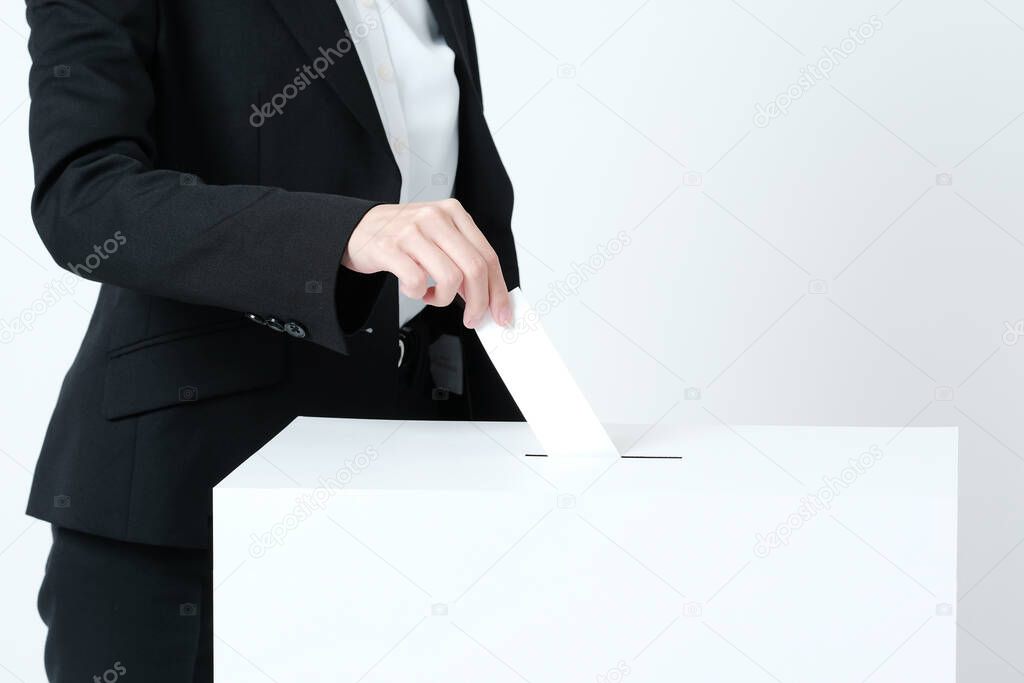 Hands of a young woman putting ballots into an election ballot box