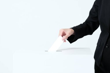 Seçim sandığına kağıt koyan takım elbiseli bir kadın eli.
