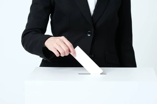 A woman\'s hand in a suit putting paper in an election ballot box