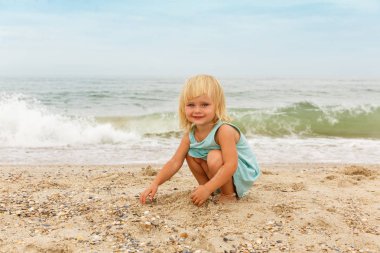 Parlak saçlı küçük bir kız ile kum deniz sahilde çalış..