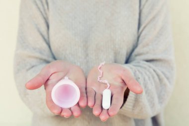 Tampon veya adet Kupası? Fem Kupası ve tampon tutan kadınsı bir el. Seçici odak.