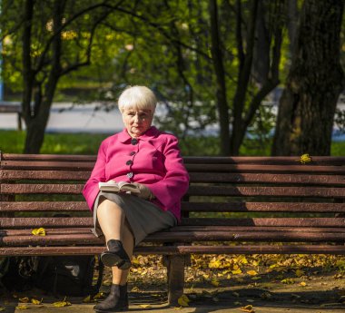 Kentsel bir parkta bir bankta oturmuş bir güzel gülümseyen emekli. O bir kitap ve bir fincan kahve tutar.