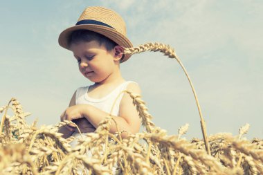 Mutlu bir aile. Küçük sevimli mutlu çocuk şapka içinde buğday alanında güler. Önden görünüm.