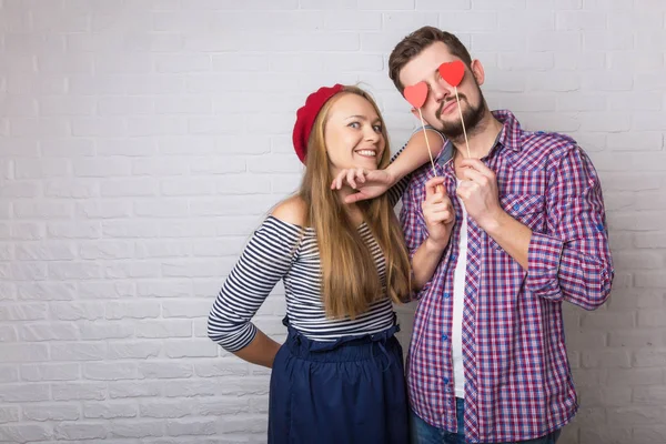 A happy funny couple in love enjoys Valentine's Day. A man with a beard and a woman with blond long hair. Paper red hearts. Loft style.