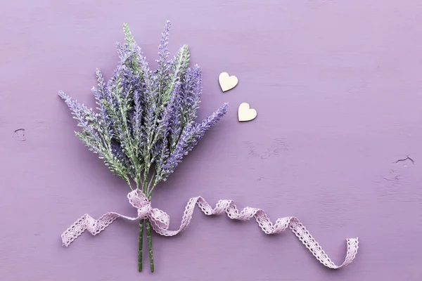 Lavender flower banded ribbon with bow on purple wooden background. Near two wooden hearts.