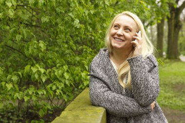 Güzel sarışın kadın 45 yaşında bir cep telefonu üzerinde şehir parkı görüşmelerde gülümseyen.