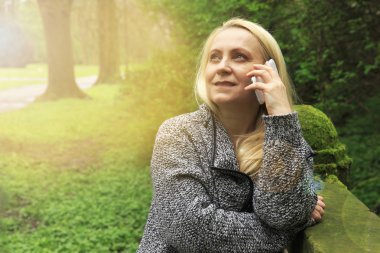 Güzel sarışın kadın 45 yaşında bir cep telefonu üzerinde şehir parkı görüşmelerde gülümseyen.