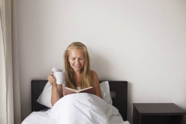Kahve ve yatakta kitap olan kadın.