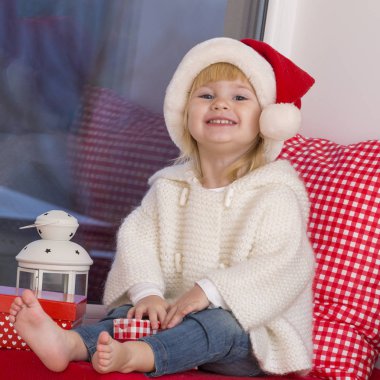 Mutlu bir aile. Bir Noel Baba'nın şapkalı küçük bir kız bir pencere pervazına penceresinde oturur ve saint için bekler.