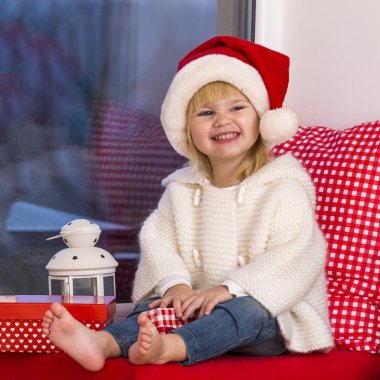 Mutlu bir aile. Bir Noel Baba'nın şapkalı küçük bir kız bir pencere pervazına penceresinde oturur ve saint için bekler.