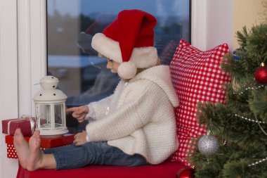 Mutlu bir aile. Bir Noel Baba'nın şapkalı küçük bir kız bir pencere pervazına penceresinde oturur ve saint için bekler.