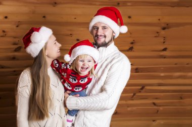 Mutlu bir aile. Anne, baba ve Noel Baba'nın şapkalı ahşap arka plan üzerinde küçük kızı.