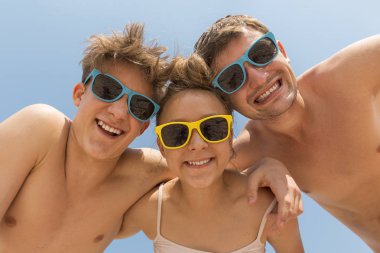 Mutlu bir aile. Baba ve genç çocuklarda iki renkli güneş gözlükleri, sarılmak, Görüntüleyici ve gülmek bak. Geniş açı.