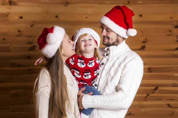 Mutlu bir aile. Anne, baba ve Noel Baba'nın şapkalı ahşap arka plan üzerinde küçük kızı.
