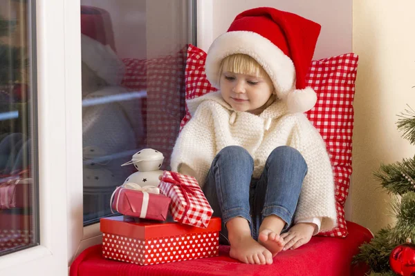 Mutlu bir aile. Bir Noel Baba'nın şapkalı küçük bir kız bir pencere pervazına penceresinde oturur ve saint için bekler.