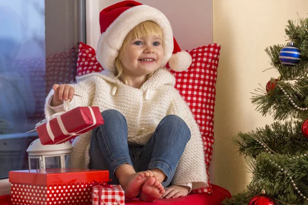 Mutlu bir aile. Bir Noel Baba'nın şapkalı küçük bir kız bir pencere pervazına penceresinde oturur ve saint için bekler.