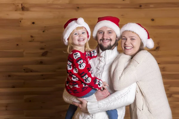 Mutlu bir aile. Anne, baba ve Noel Baba'nın şapkalı ahşap arka plan üzerinde küçük kızı.
