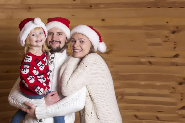 Mutlu bir aile. Anne, baba ve Noel Baba'nın şapkalı ahşap arka plan üzerinde küçük kızı.