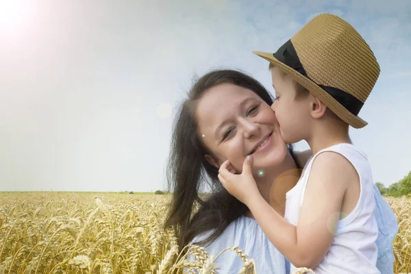 Mutlu bir aile. Anne ve oğlu gülüyor ve buğday sahada konuşuyor. Önden görünüm.