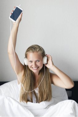 Genç Sarışın ve mutlu gülümseyen kadın müzik dinlemek ve kahve beyaz yatakta sabah zamanında.