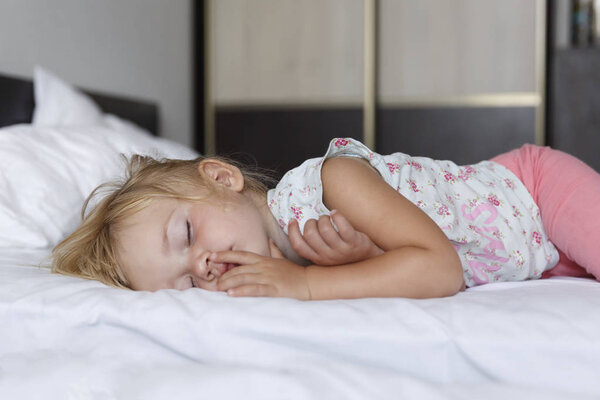 Sweet little blond girl sleeps in bed with her parents. White background.