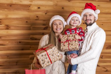 Mutlu bir aile. Anne, baba ve küçük kızı ile Noel Baba'nın şapkalı sunar bir ahşap arka plan üzerinde.