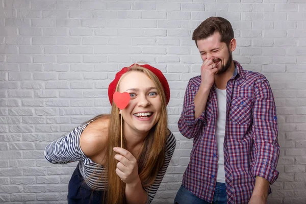 A happy funny couple in love enjoys Valentine\'s Day. A man with a beard and a woman with blond long hair. Paper red hearts. Loft style.