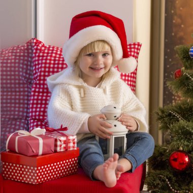 Mutlu bir aile. Bir Noel Baba'nın şapkalı küçük bir kız bir pencere pervazına penceresinde oturur ve saint için bekler.